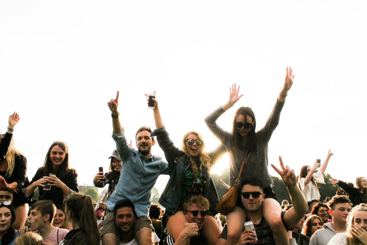 Friends cheering with arms raised on shoulders in a sunny outdoor festival crowd